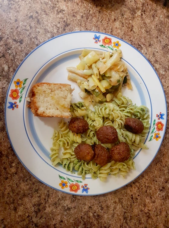Plate of food with pesto pasta, vegan meatballs, zucchini and wax beans, and mango coffee cake