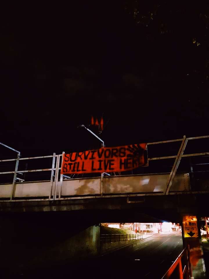 banner with text 'survivors still live here' hanging from 'living bridge' over 97 street and 105 ave.